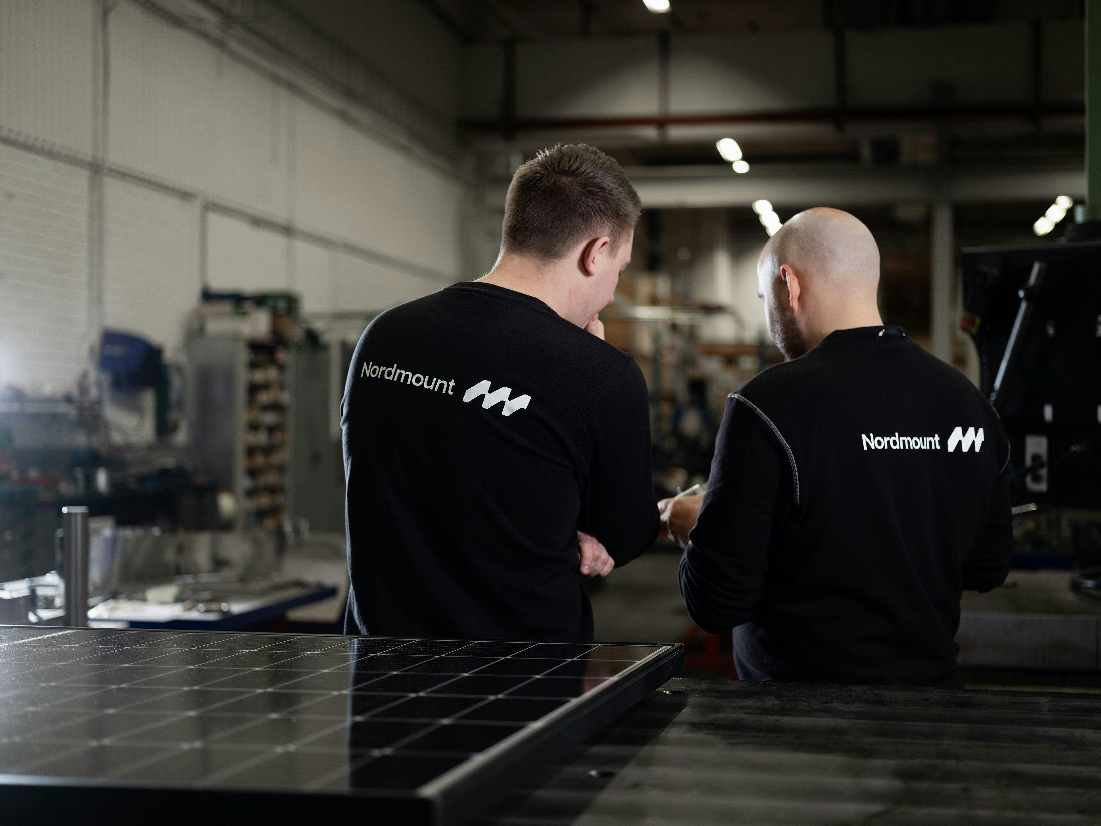 Två medarbetare på Nordmount bakom solcellspaneler